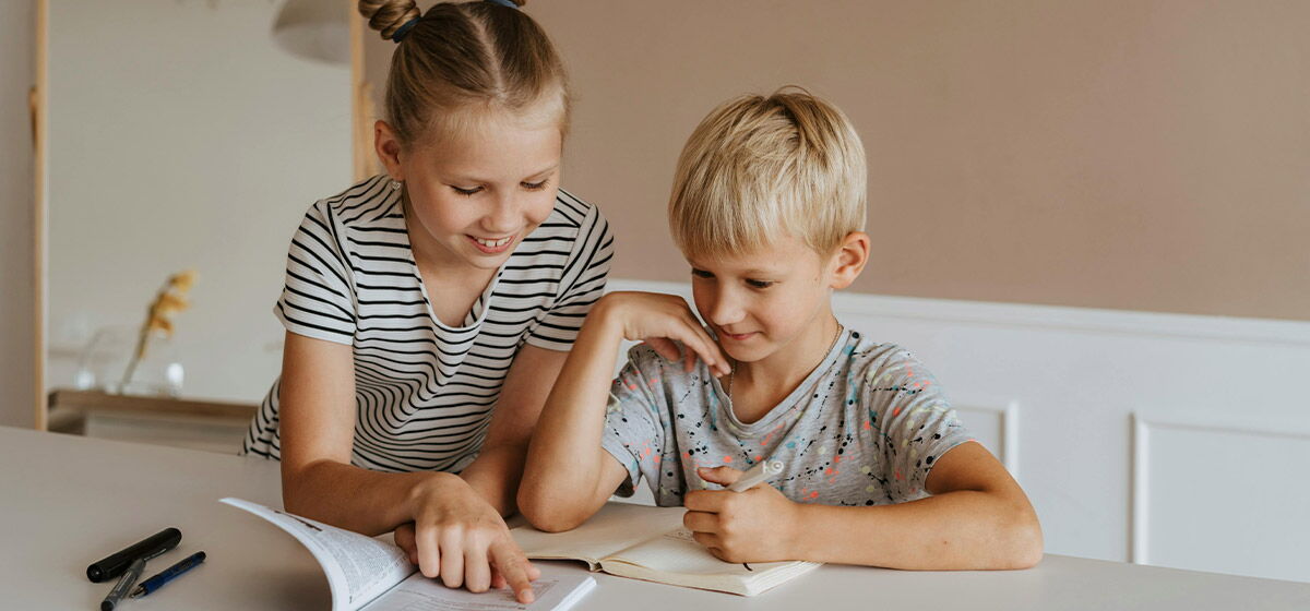 Ein Mädchen bring einem Jungen am Schreibtisch das lesen bei. Gebäugt über ein Buch