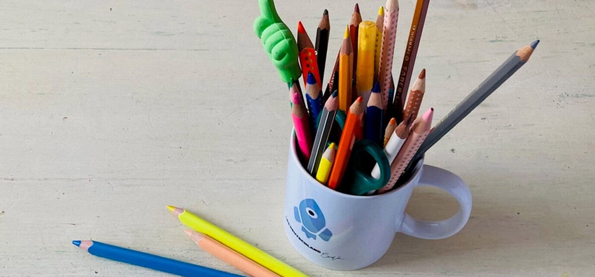 Weiße Tasse mit blauem LRS Deutschland Logo darauf und die Tasse ist gefüllt mit Buntstiften